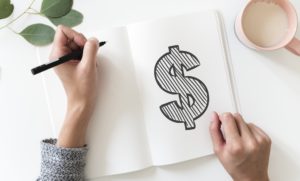 A woman drawing a dollar sign in a notebook.